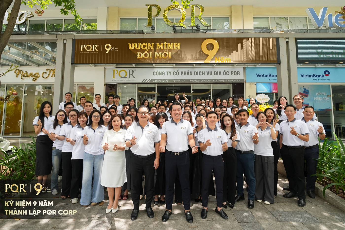 Toàn thể đội ngũ PQR Corp chụp ảnh kỷ niệm 9 năm thành lập trước văn phòng, với backdrop